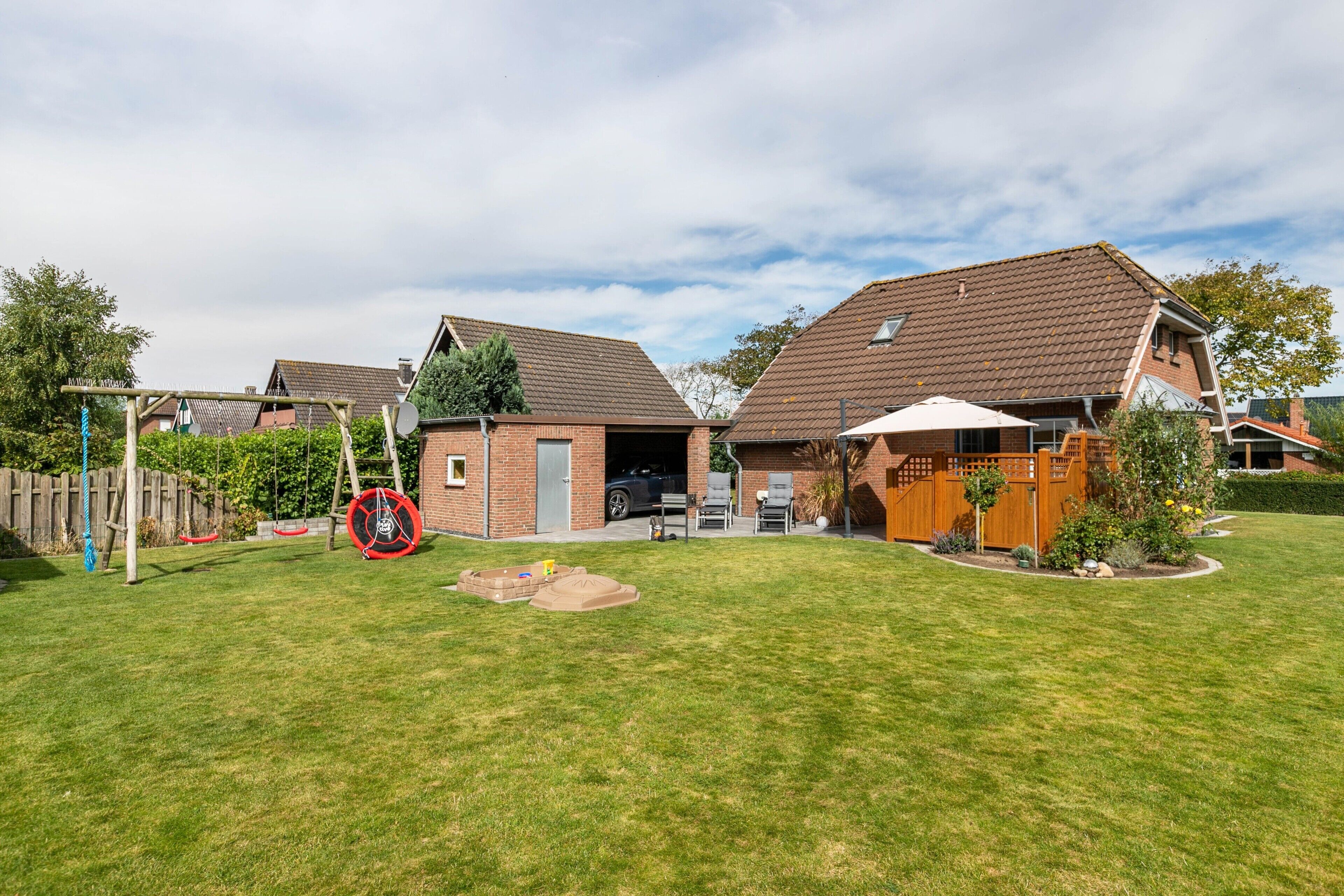 Ein Wohnhaus mit eingezäunter Garten, einer Holzterrasse und einer Garage.