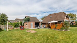 Een woonhuis met een omheinde achtertuin, een houten terras en een garage.