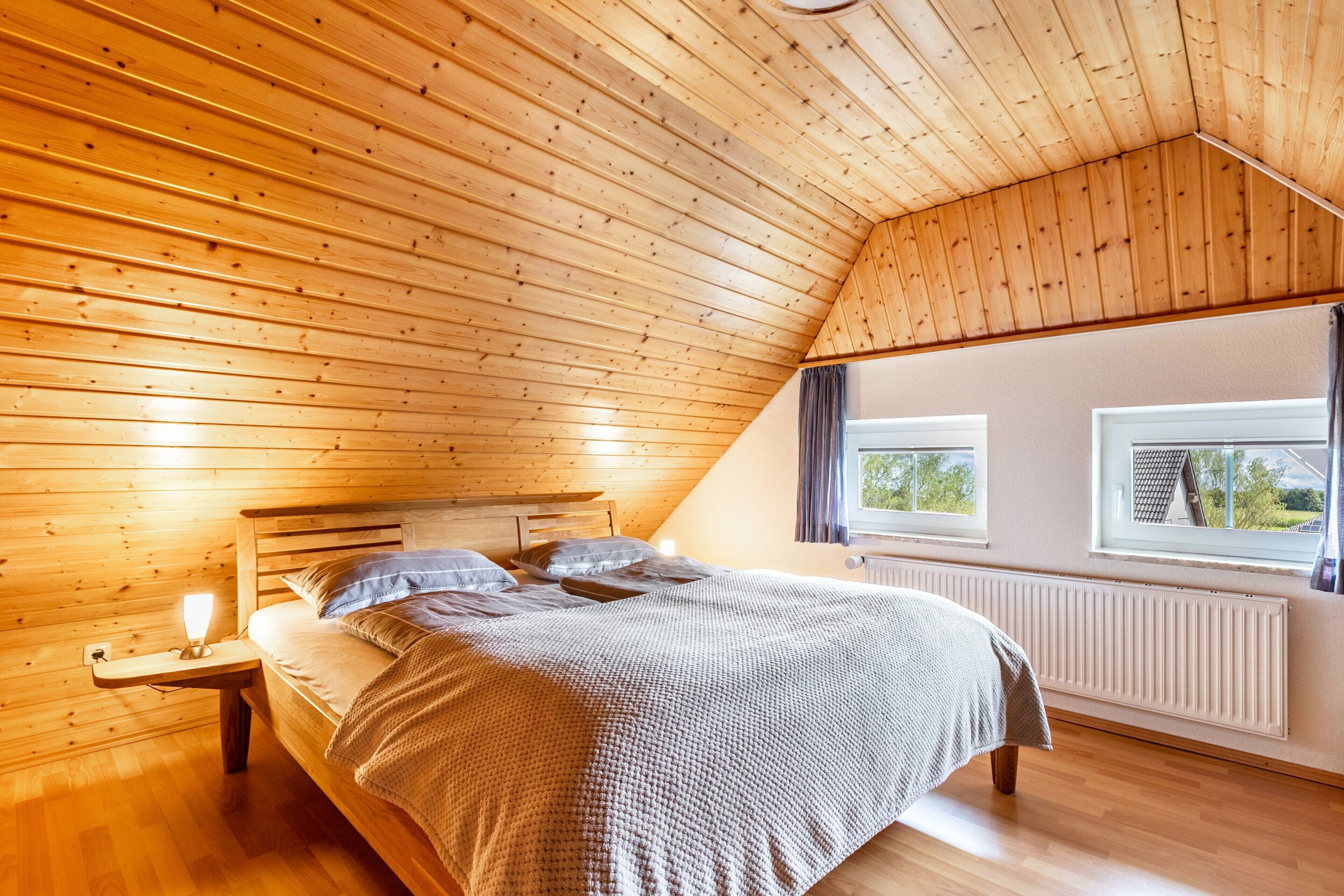 Ein Schlafzimmer mit Schrägwand, einem Bett, einem Nachttisch, einem Fenster und einer Heizung.