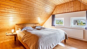 Een slaapkamer met een schuine kap, een bed, een nachtkastje, een raam en een radiator.