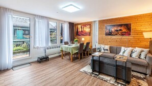 A modern living room with a dining area, wooden panel walls, and large windows.