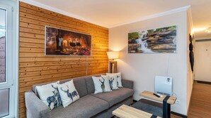 A modern living room with a gray sofa, wooden panel wall, and two framed pictures.