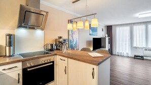 A modern kitchen with a built-in oven, a coffee machine, and a microwave. There is a wooden countertop and a hanging light fixture.
