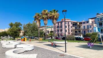 A paved plaza with a circular seating area, palm trees, and multi-story buildings in the background.