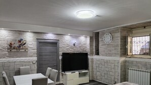 Habitació amb taula de dinar i cadires, televisió, llit i finestra amb reixes.