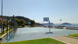 Una pista de bàsquet a l'aire lliure amb vista despejada a la mar i les colines al fons.