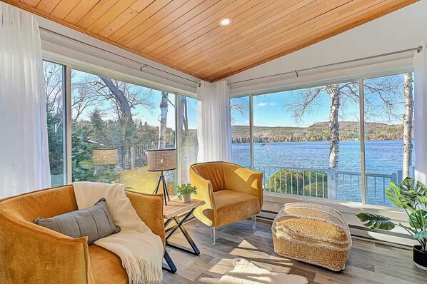 A modern living room with large windows, a wooden ceiling, and a view of a lake. - Waterfront with Spa and Lake Access (Saint-Damien)