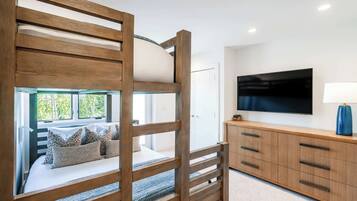 A bunk bed with a view of greenery, a TV on the wall, and a wooden cabinet with drawers.