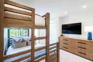 A bunk bed with a view of greenery, a TV on the wall, and a wooden cabinet with drawers.