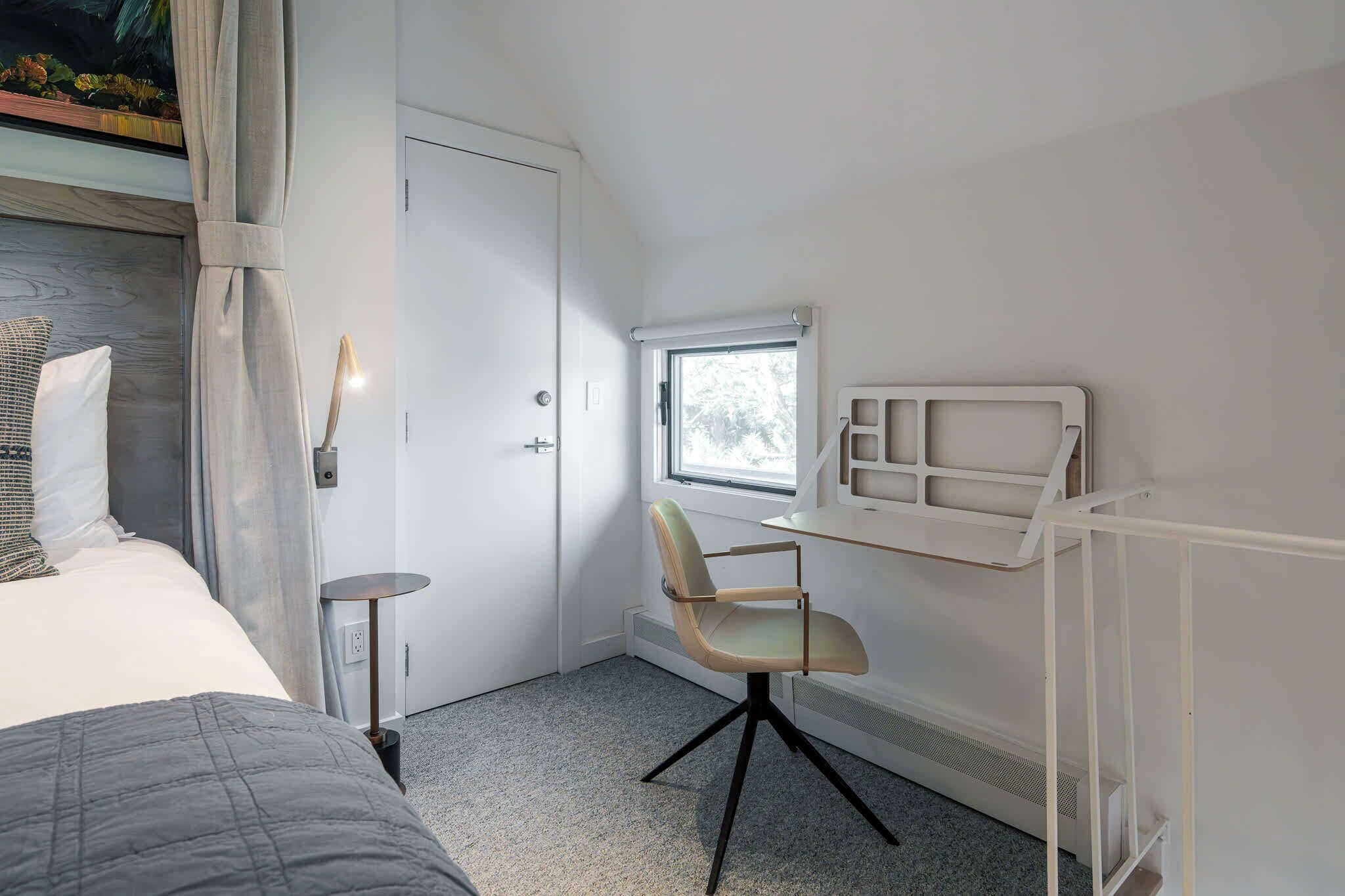 Una camera da letto con un letto, una scrivania con una sedia, una finestra e un termosifone.