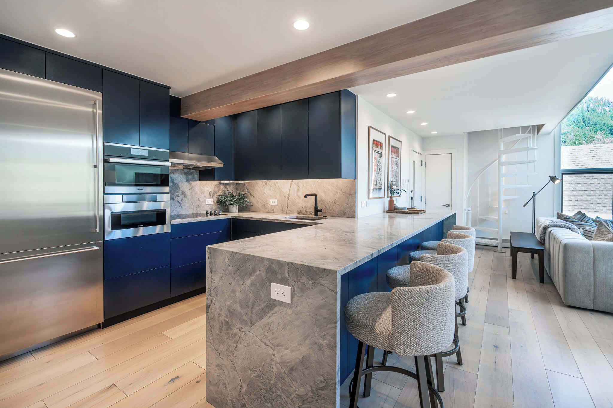 Een moderne keuken met donkerblauwe kastjes, een roestvrijstalen koelkast en een marmeren kookeiland met barstoelen.