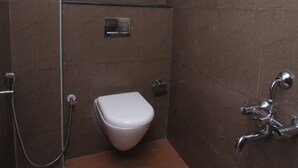 A small, compact bathroom with a white toilet, a shower area, and a small window. - Golden Tower (Chennai)