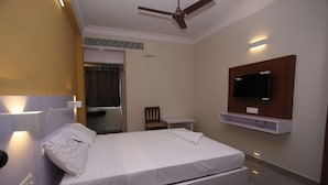 A modern hotel room with a single bed, a TV mounted on the wall, a ceiling fan, and a small bedside table. - Golden Tower (Chennai)