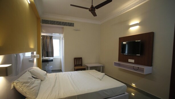 A hotel room with a bed, a TV mounted on the wall, a ceiling fan, and a small table. - Golden Tower (Chennai)