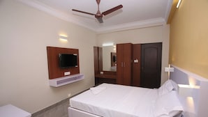 A hotel room with a bed, a TV mounted on the wall, a wardrobe, and a ceiling fan. - Golden Tower (Chennai)