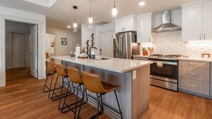 A modern kitchen with a central island, bar stools, stainless steel appliances, and pendant lighting. - TimberFox 3209 | 2BR Downtown, Hot Tub, A/C (Winter Park)