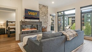A modern living room with a fireplace, a sofa, and a large window. - TimberFox 3209 | 2BR Downtown, Hot Tub, A/C (Winter Park)