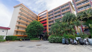 A multi-story building with balconies, surrounded by greenery and parked scooters. - Condo Gym Plane Views Near Beach C172 (Mai Khao)