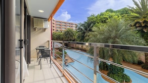 A balcony with a pool, surrounded by lush greenery and a view of a building in the background. - Condo Gym Plane Views Near Beach C172 (Mai Khao)