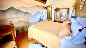 Ein Schlafzimmer mit Bergbild, Holzbalken, einem Holzschrank und einem Bett mit weißer Bettwäsche.
