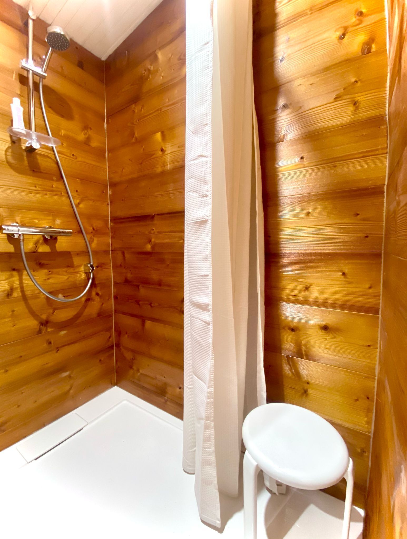 A wooden cabin bathroom with a shower, toilet, and a small stool.