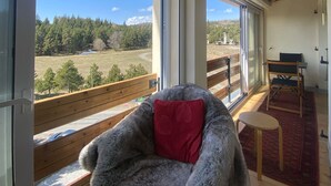 Ein gemütliches Zimmer mit großem Fenster, einem bequemen Sessel, einem kleinen Tisch und einer Bank draußen.