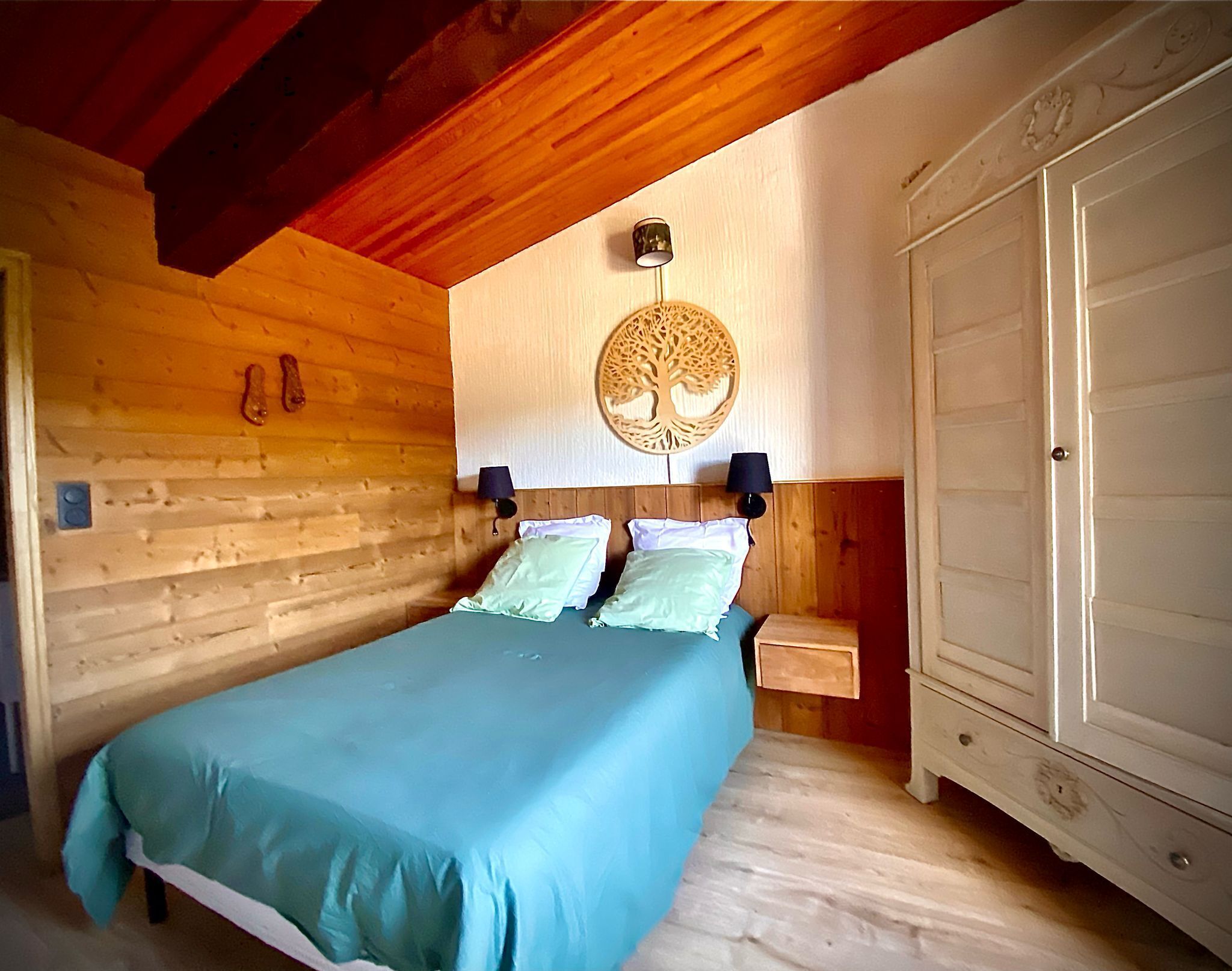 A wooden cabin bedroom with a bed, two bedside tables, a wardrobe, and a decorative wall hanging.