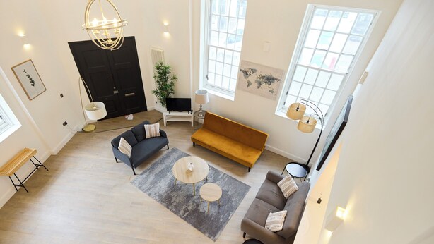 A spacious living area with a dark sofa, a wooden bench, a round coffee table, and a large window. - Central Tadworth Flat (Tadworth)