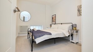 A bedroom with a bed, a bedside table with a lamp, a radiator, and a framed picture on the wall. - Central Tadworth Flat (Tadworth)