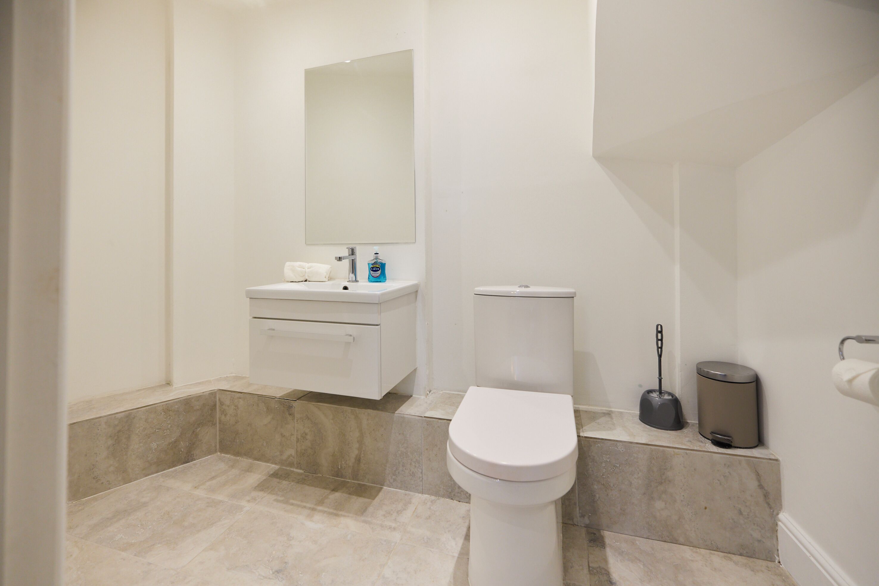 A bathroom with a toilet, sink, mirror, and a trash bin.