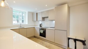 A modern kitchen with white cabinetry, a built-in oven, a sink, and a window providing natural light. - Central Tadworth Flat (Tadworth)