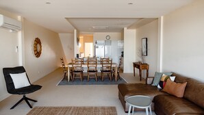 A modern living room with a brown leather sofa, a black chair, and a dining area with wooden chairs and a table. - Sandy Nook - 2/192B Griffiths Street (Port Fairy)