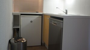 Uma cozinha compacta com máquina de lavar louça, pia e lixeira.