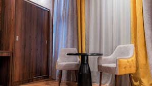 A room with a wooden wardrobe, a round black table, two upholstered chairs, and a yellow curtain.