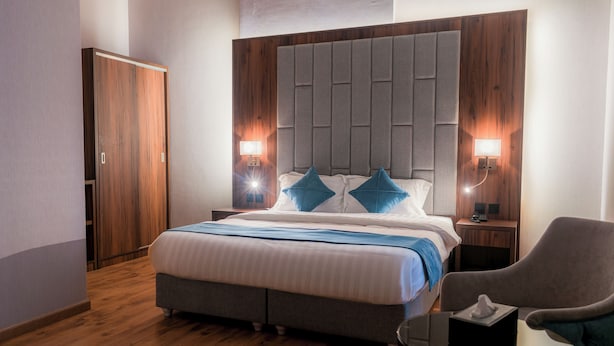 A bedroom with a large bed, wooden wardrobe, two bedside lamps, and a chair.