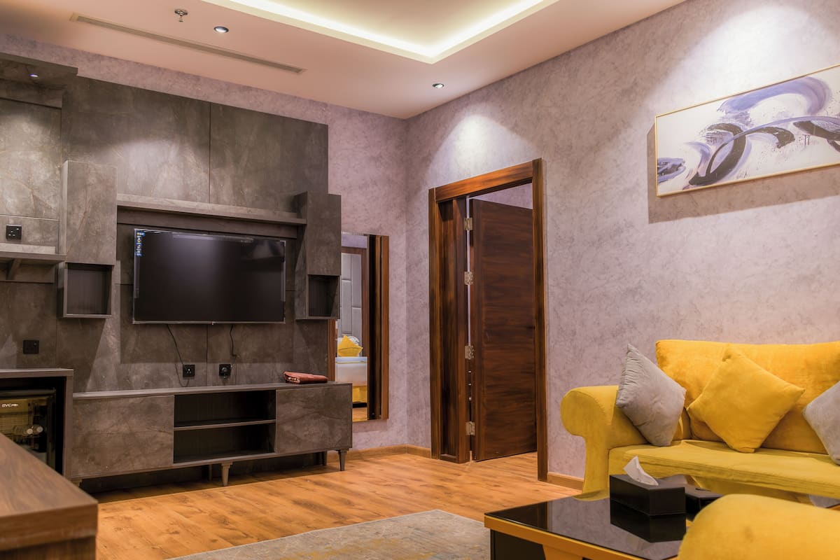 Ein modernes Wohnzimmer mit Flachbildfernseher, einer Holzunterhaltungsecke und einem gelben Sofa.