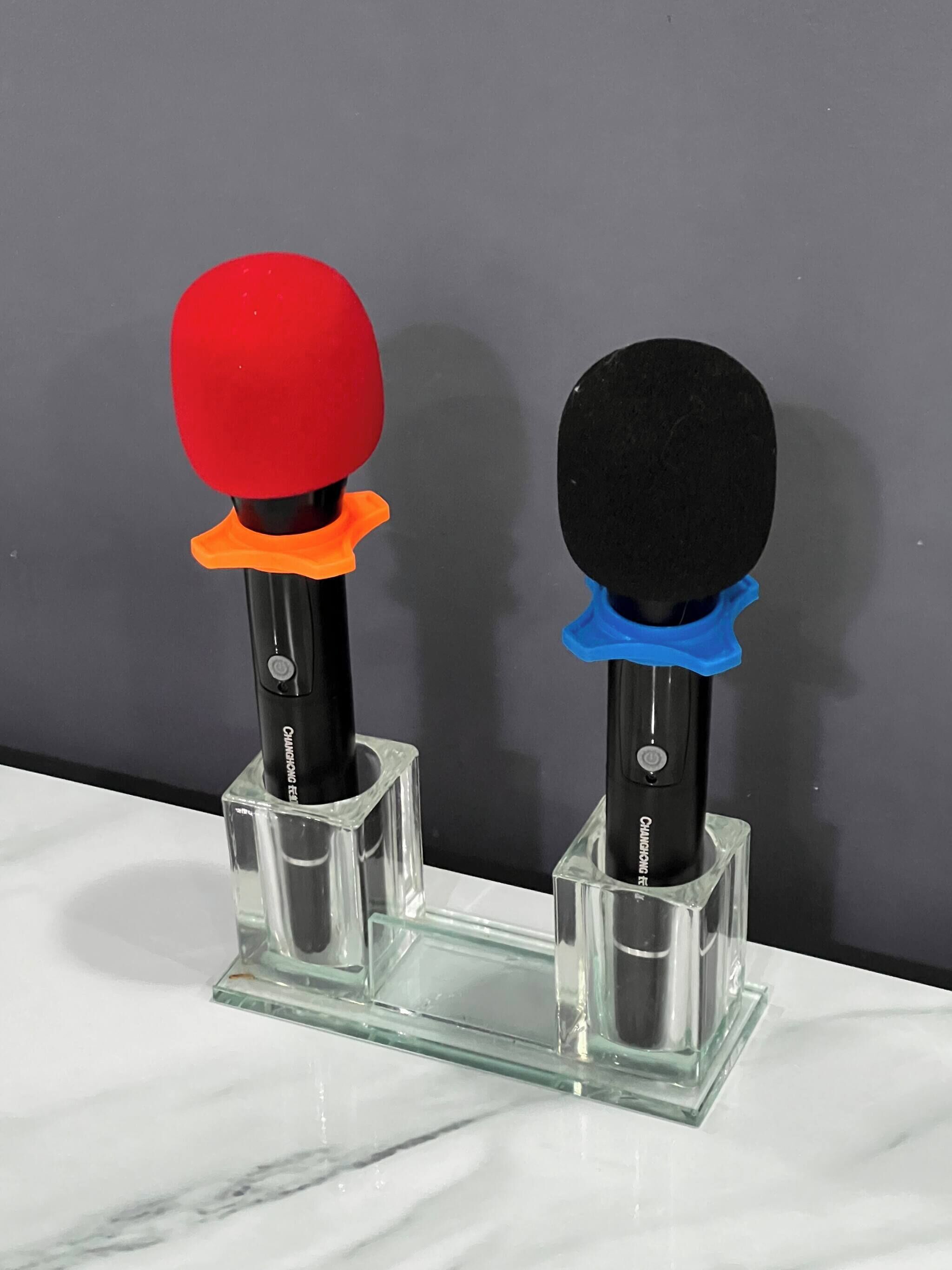 Two ping pong paddles on a clear glass stand against a grey wall.