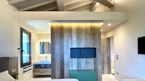 Une chambre moderne avec un grand lit, une banquette intégrée, une coiffeuse avec un miroir et un téléviseur fixé au mur.