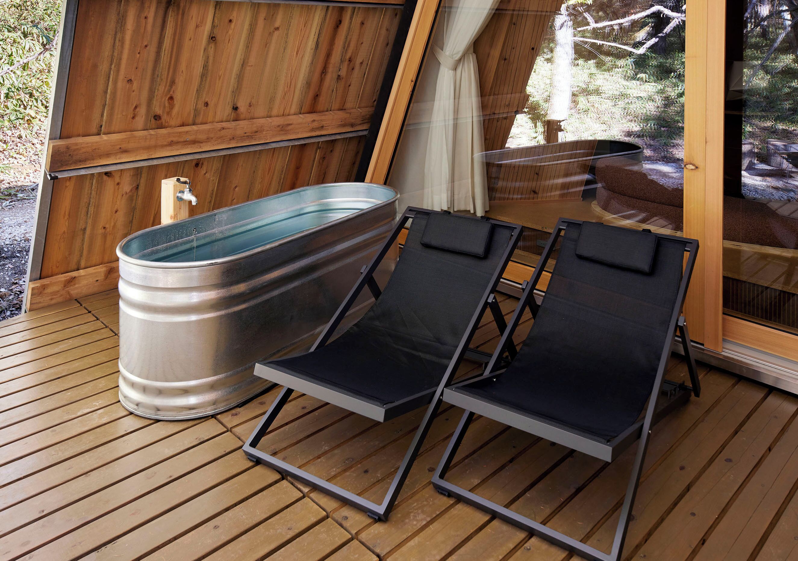 Une terrasse en bois avec deux chaises longues noires et un jacuzzi en métal.