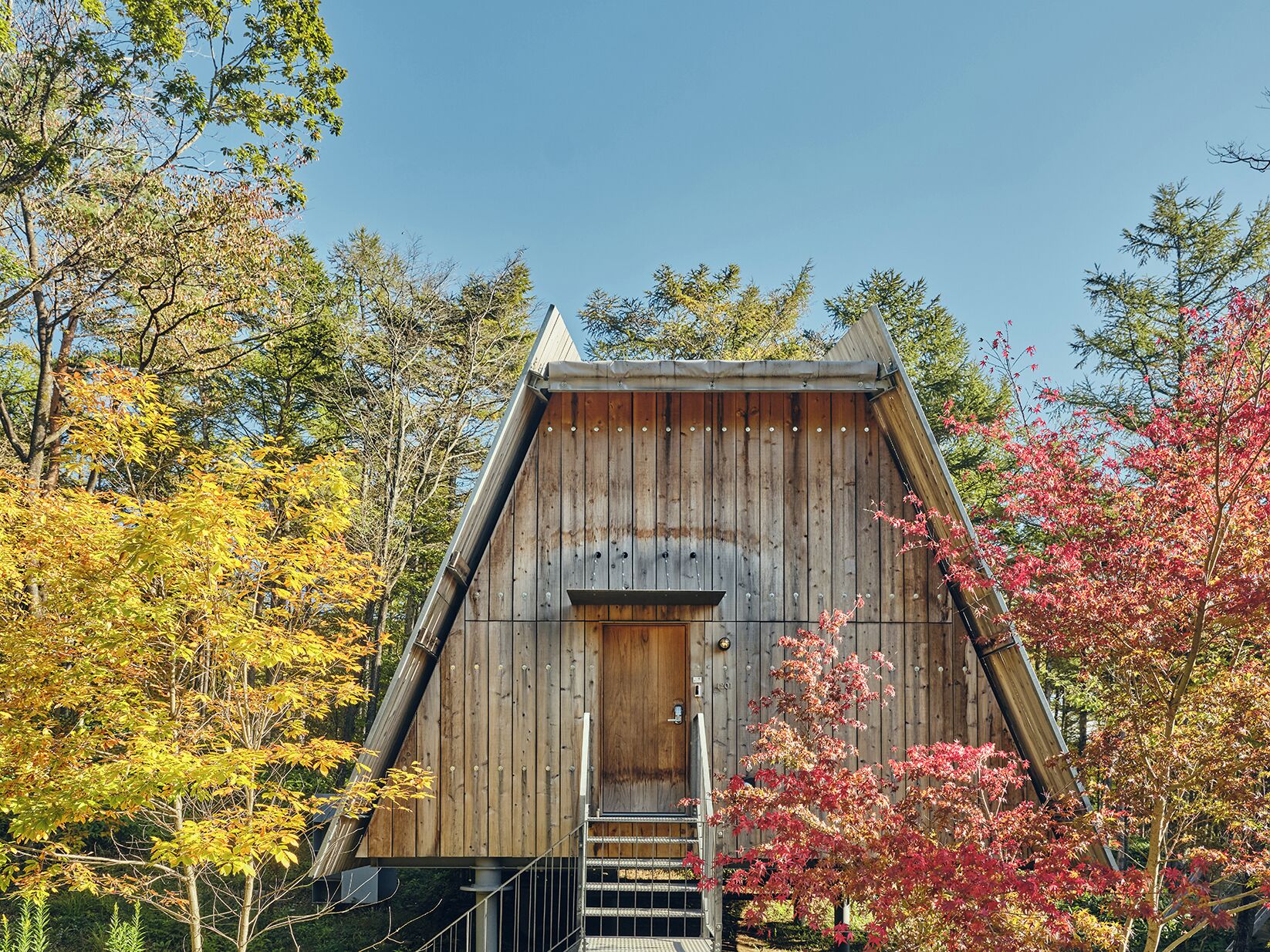 A wooden cabin with a steep roof, a front door, and a staircase leading up to the entrance.