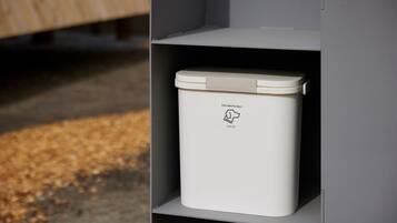 A white dog waste bin labeled "DOG WASTE ONLY" on a shelf.