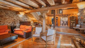 Ein geräumiger Wohnbereich mit Steinwand, Holzbalkendecke und einer Treppe zu einer oberen Ebene.