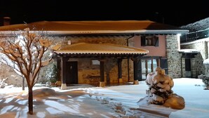 Une maison recouverte de neige, avec une façade en pierre, un porche en bois et une sculpture de neige.
