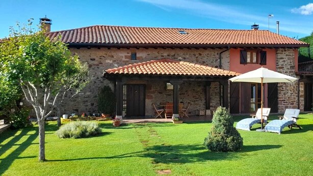 Une maison en pierre avec un toit en tuiles, un patio couvert avec des meubles d’extérieur et une pelouse bien entretenue.