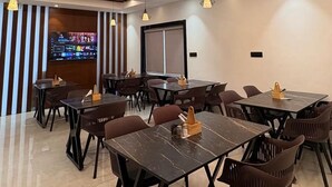 A modern dining area with multiple tables and chairs, a flat-screen TV, and a projection screen on the wall. - LEONAR HOTEL (Hyderabad)