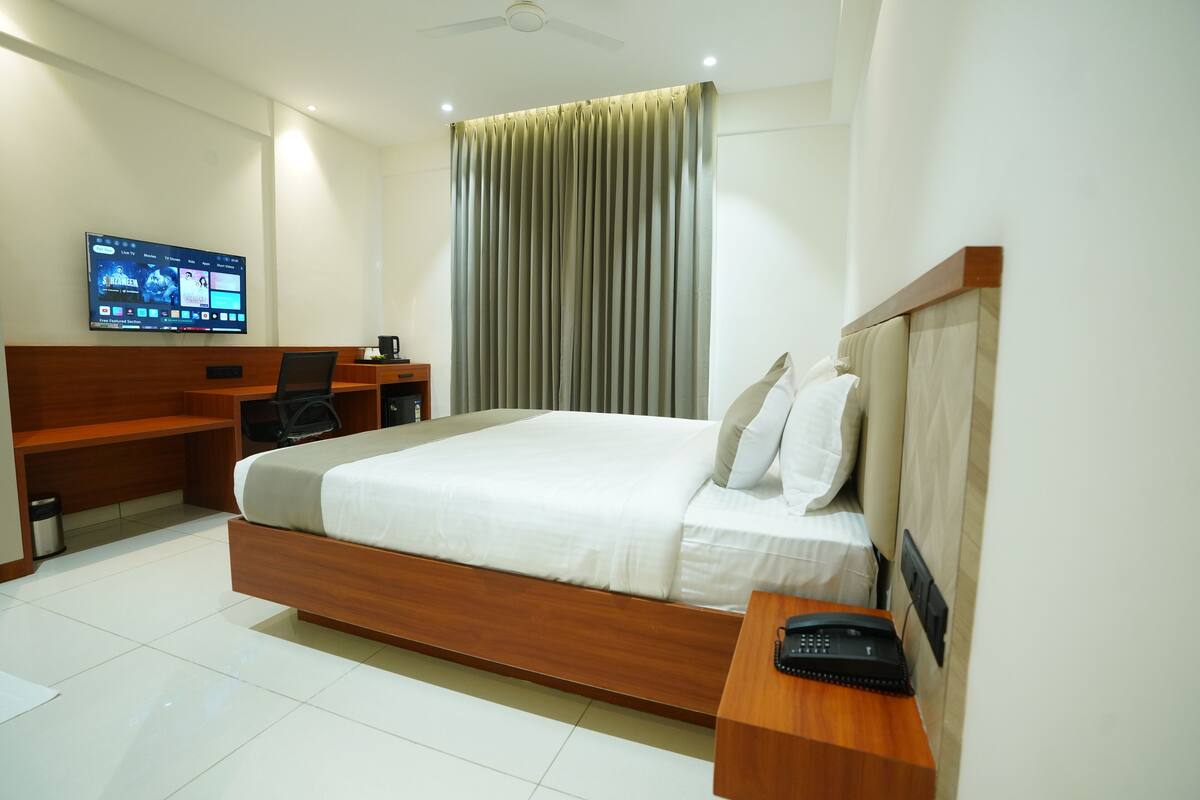 A modern hotel room with a large bed, a desk with a computer, a flat-screen TV mounted on the wall, and a ceiling fan.