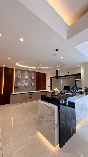 A modern kitchen with a central island, recessed lighting, and a wall-mounted clock. - LEONAR HOTEL (Hyderabad)
