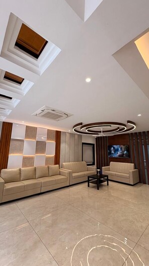 A modern living room with a sectional sofa, a coffee table, recessed ceiling lighting, and a flat-screen TV mounted on the wall. - LEONAR HOTEL (Hyderabad)