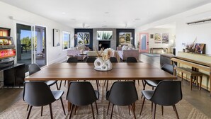 A spacious dining area with a long wooden table, black chairs, and a piano. - Hoopa House by Fieldtrip - Pickleball + 2 Pools (Yucca Valley)