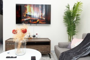 Un soggiorno con televisore a parete, un mobile porta TV in legno, un divano grigio e una grande pianta verde.